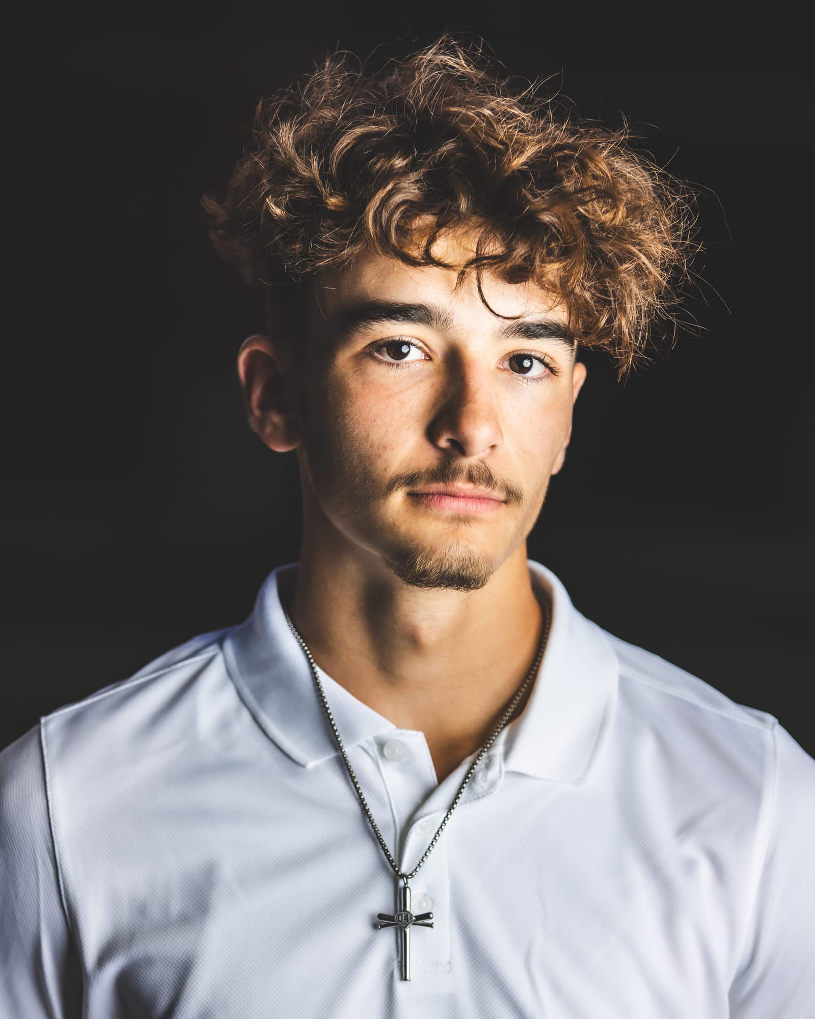 Studio portrait of a senior in a white collared shirt against a near-black ground, lit from one side.