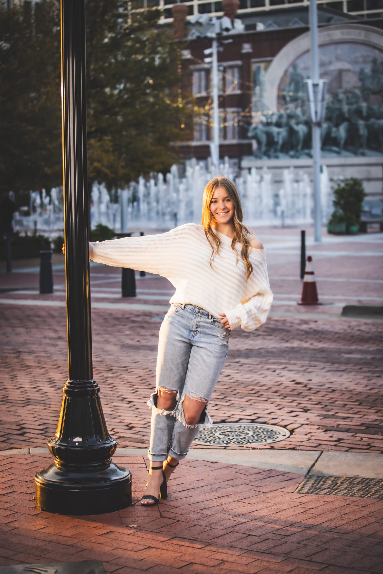 A senior leaning against a cast-iron lamppost on a brick downtown plaza, arm outstretched.