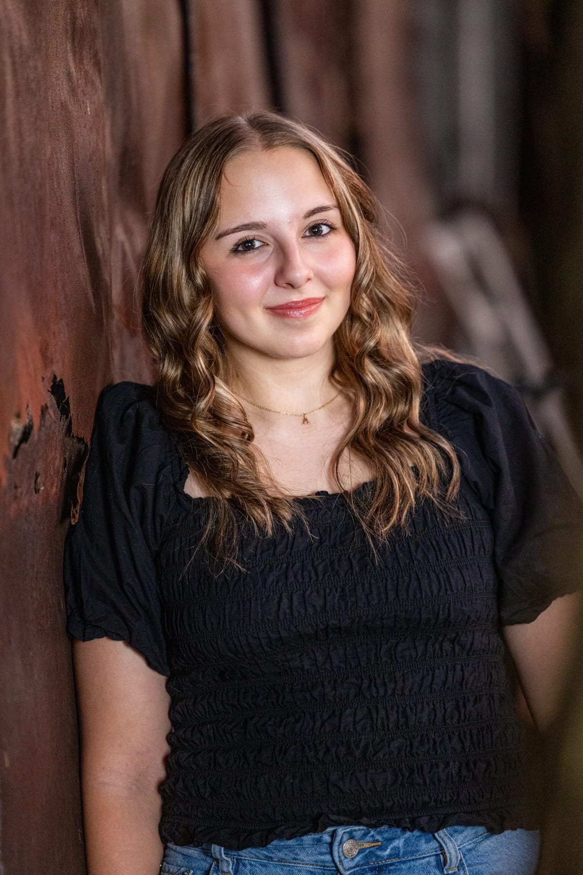 A senior against a wall of weathered barn wood, arms loose at her sides.