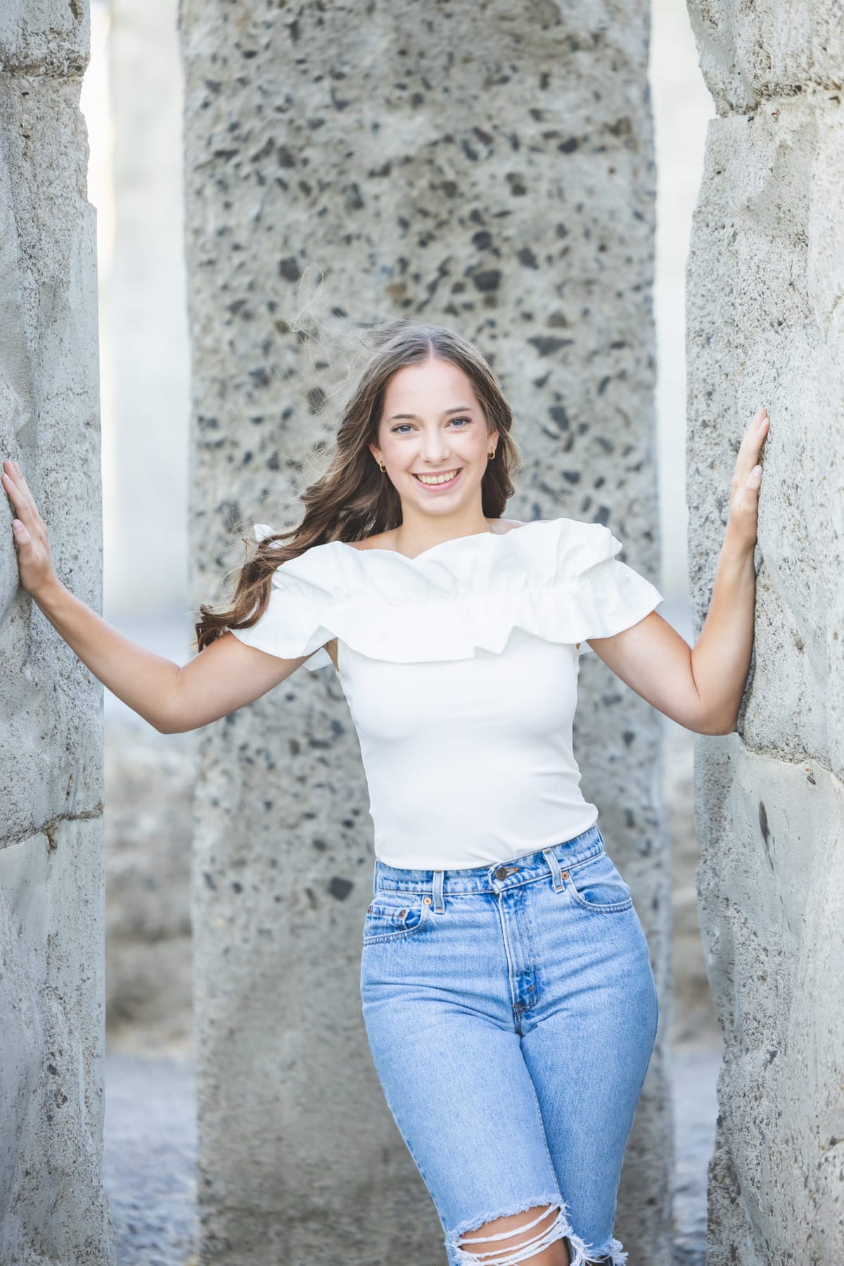 A senior leaning between weathered stone columns, hands flat against the stone.