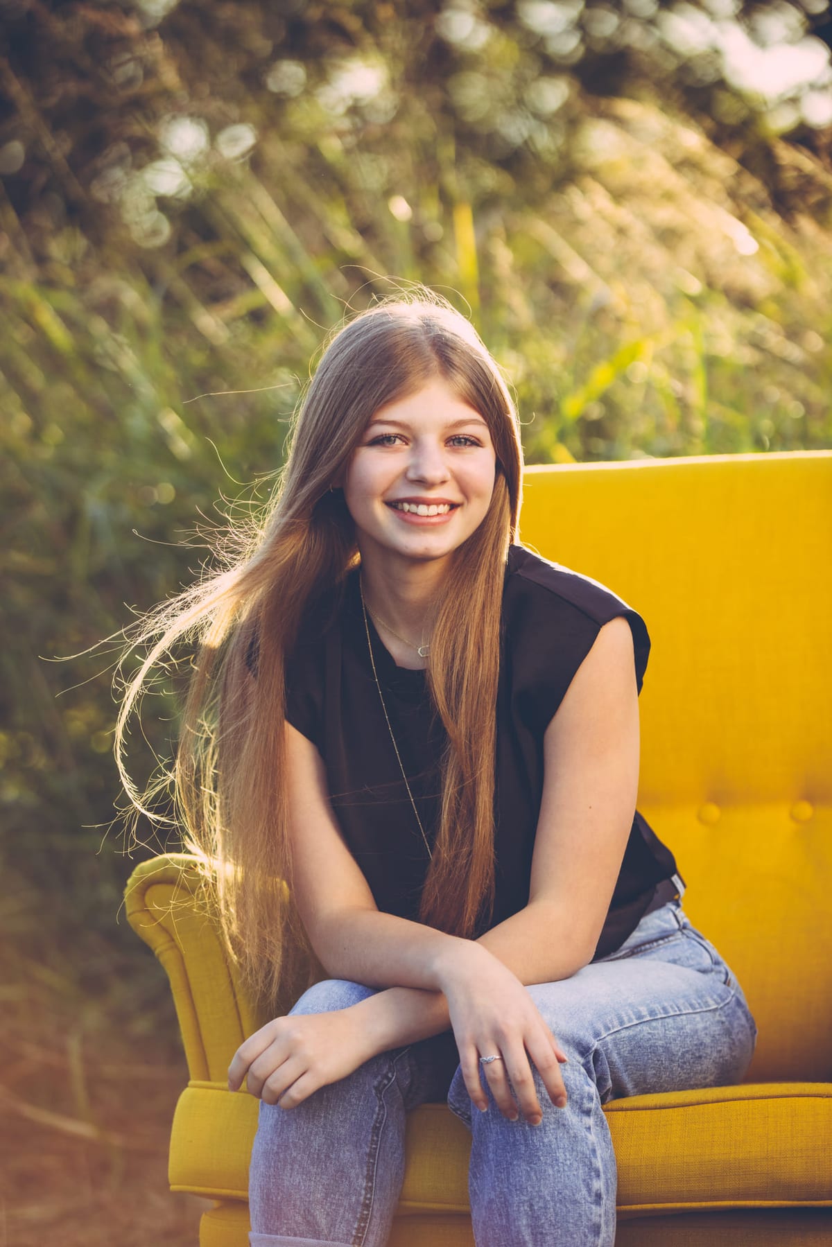 A senior sitting in a yellow armchair outdoors, backlit by sun through the leaves.