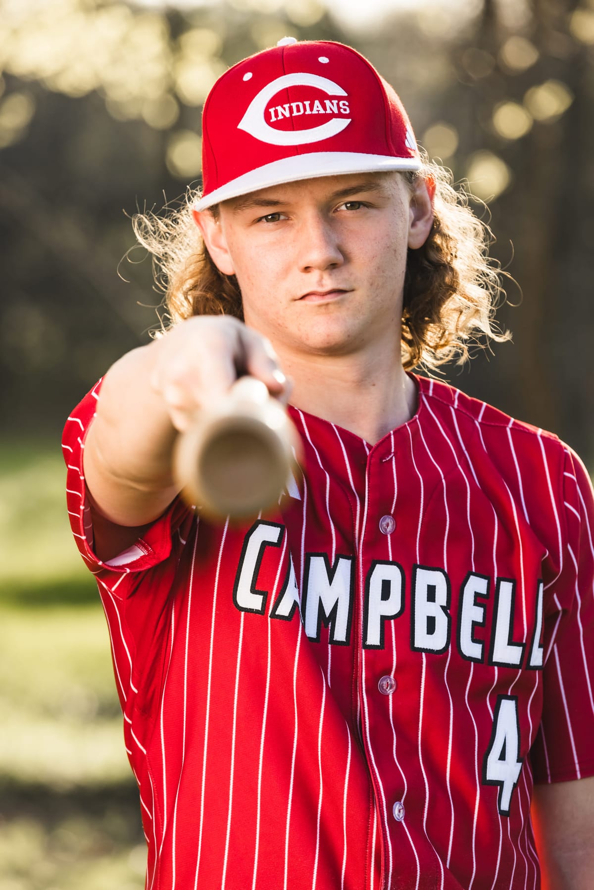 A pitcher levelling his bat straight at the camera, cap pulled low.