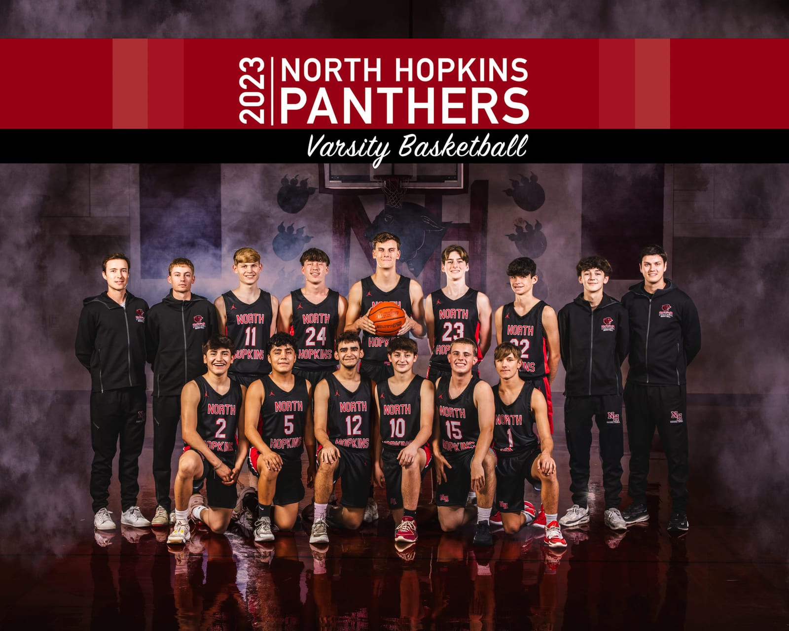 A varsity basketball team banner: the full squad posed on a reflective floor under the team’s lettering.