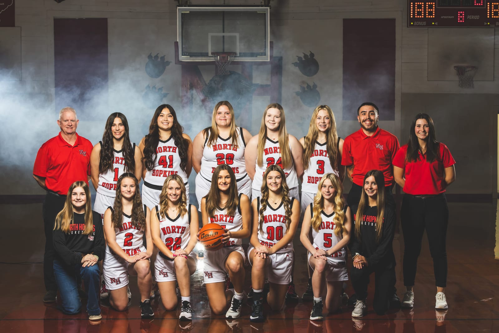 A cheer squad and its coaches posed together across the gym floor, haze in the air.