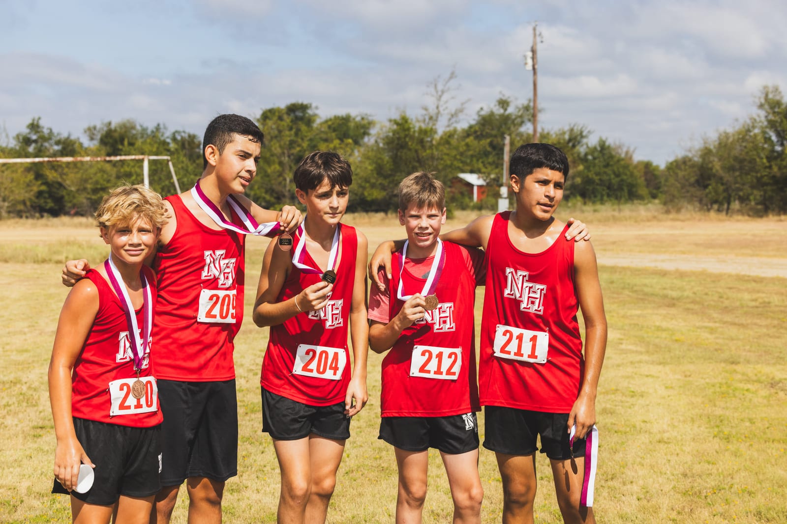Cross-country runners standing together in a field with medals around their necks.