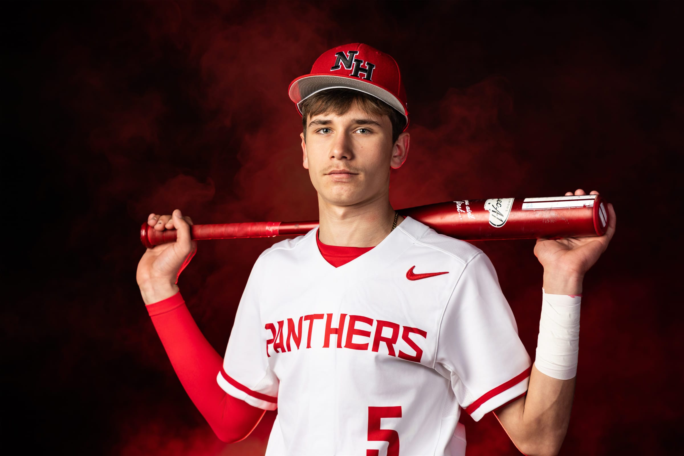 A baseball player with two bats laid across his shoulders, lit against billowing red smoke.