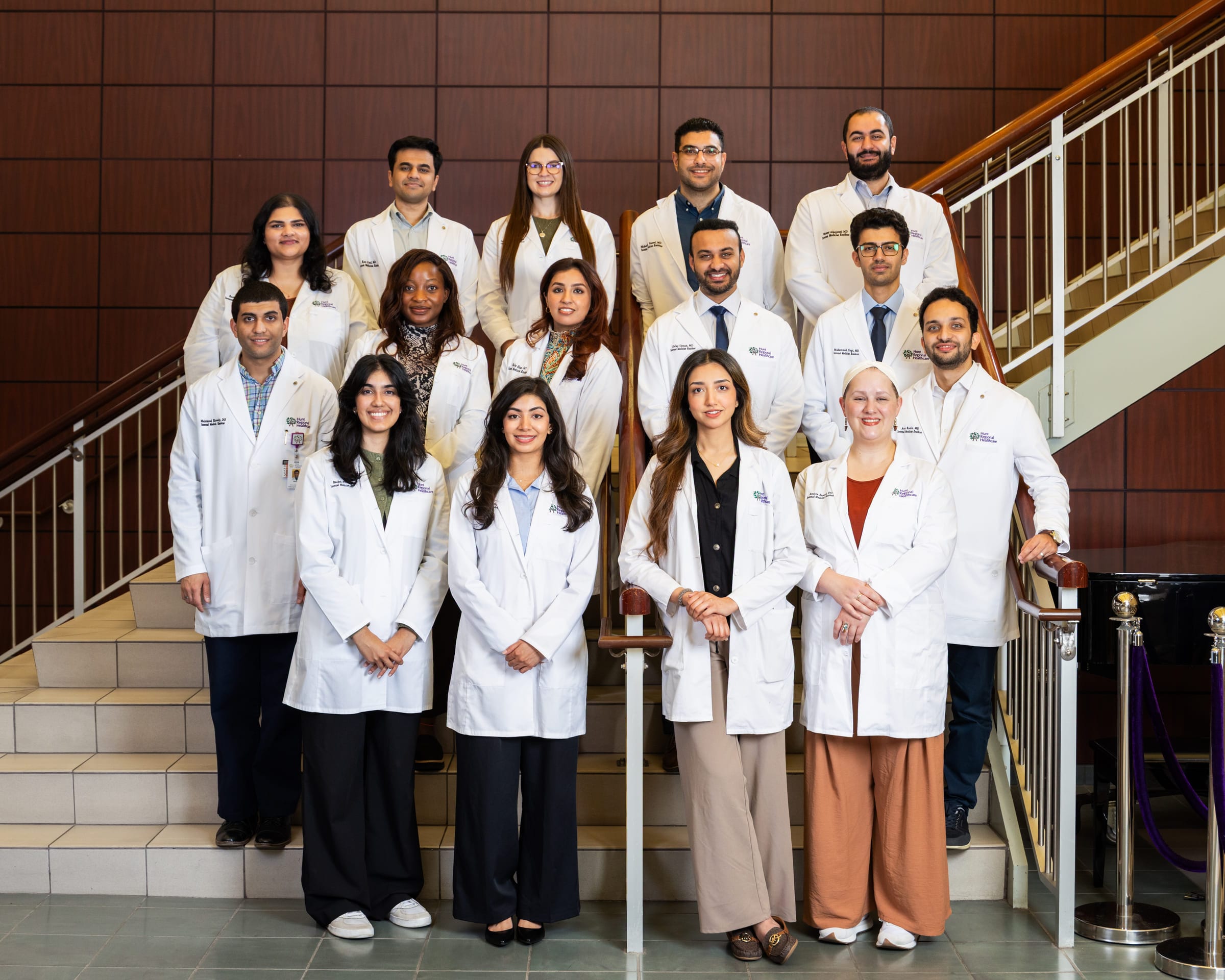 A residency class in white coats arranged in three rows on a tiled staircase.