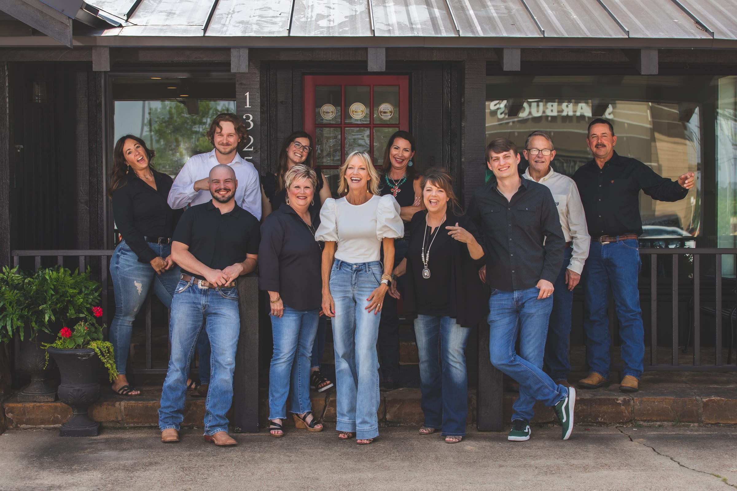 An eleven-person real-estate team standing together along the porch of their office.