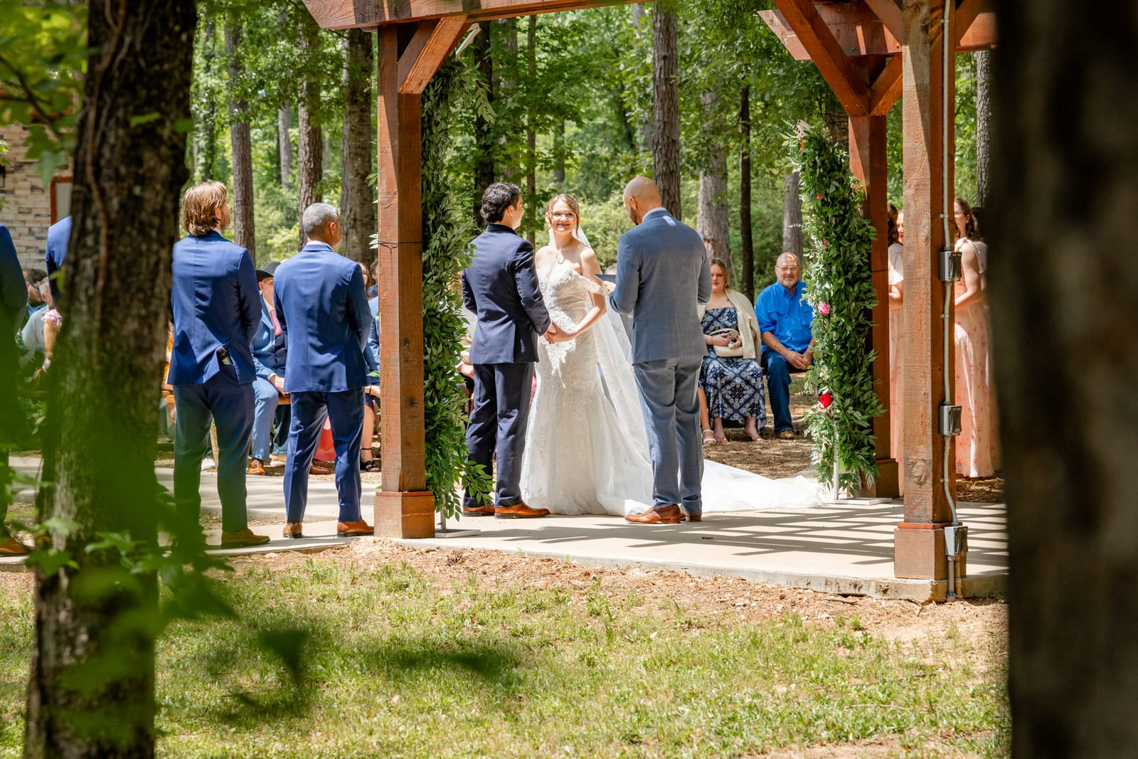 An outdoor ceremony under a timber arbor, guests standing on either side.