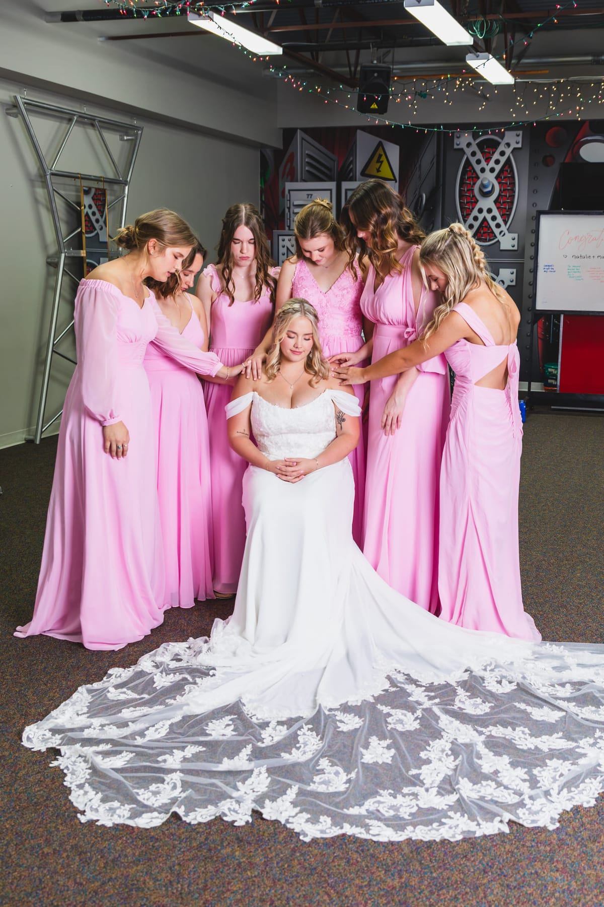 Bridesmaids in pink gathered close around the bride, her lace train spread across the floor.