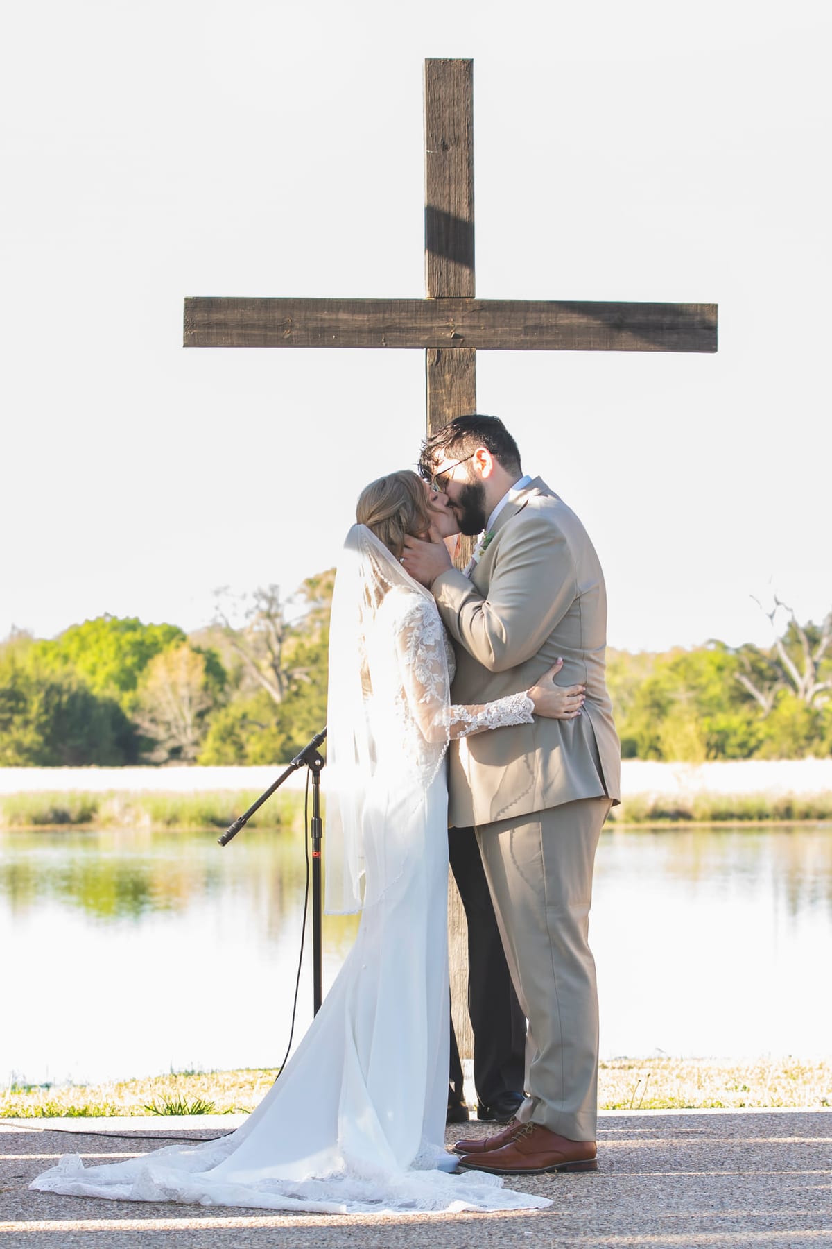 A couple facing each other at a wooden cross by the water at the close of the ceremony.