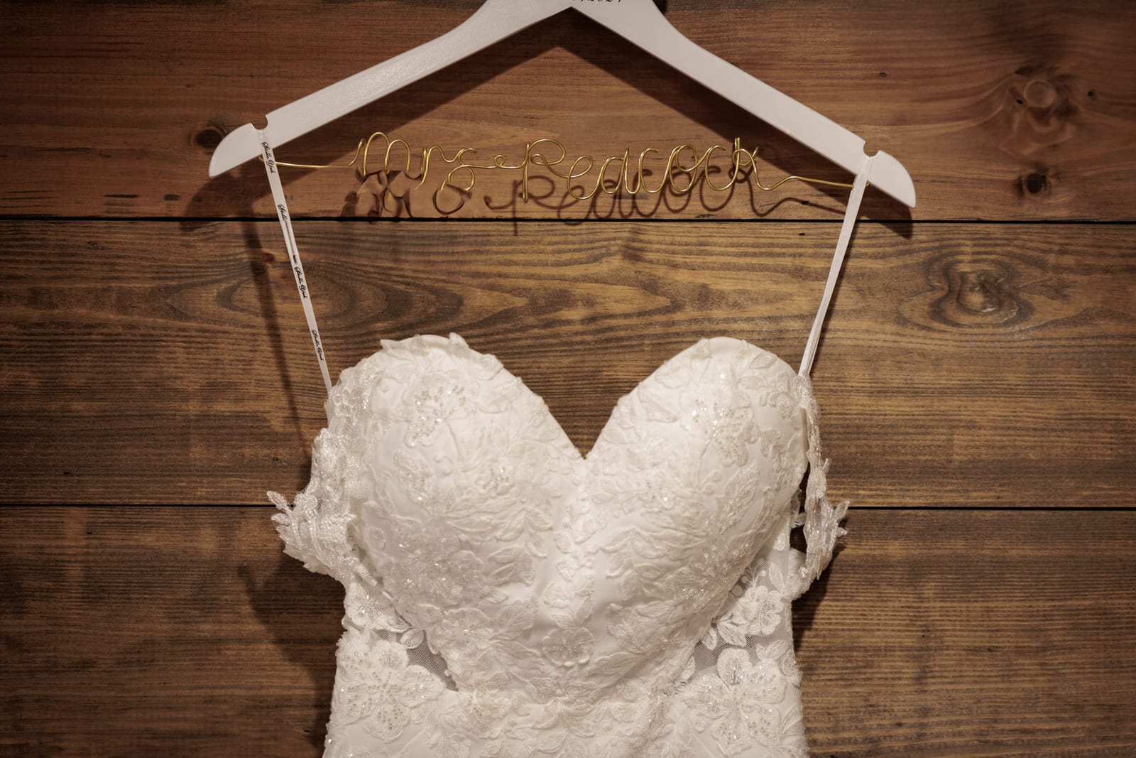 A wedding gown on a lettered wooden hanger against barn boards.