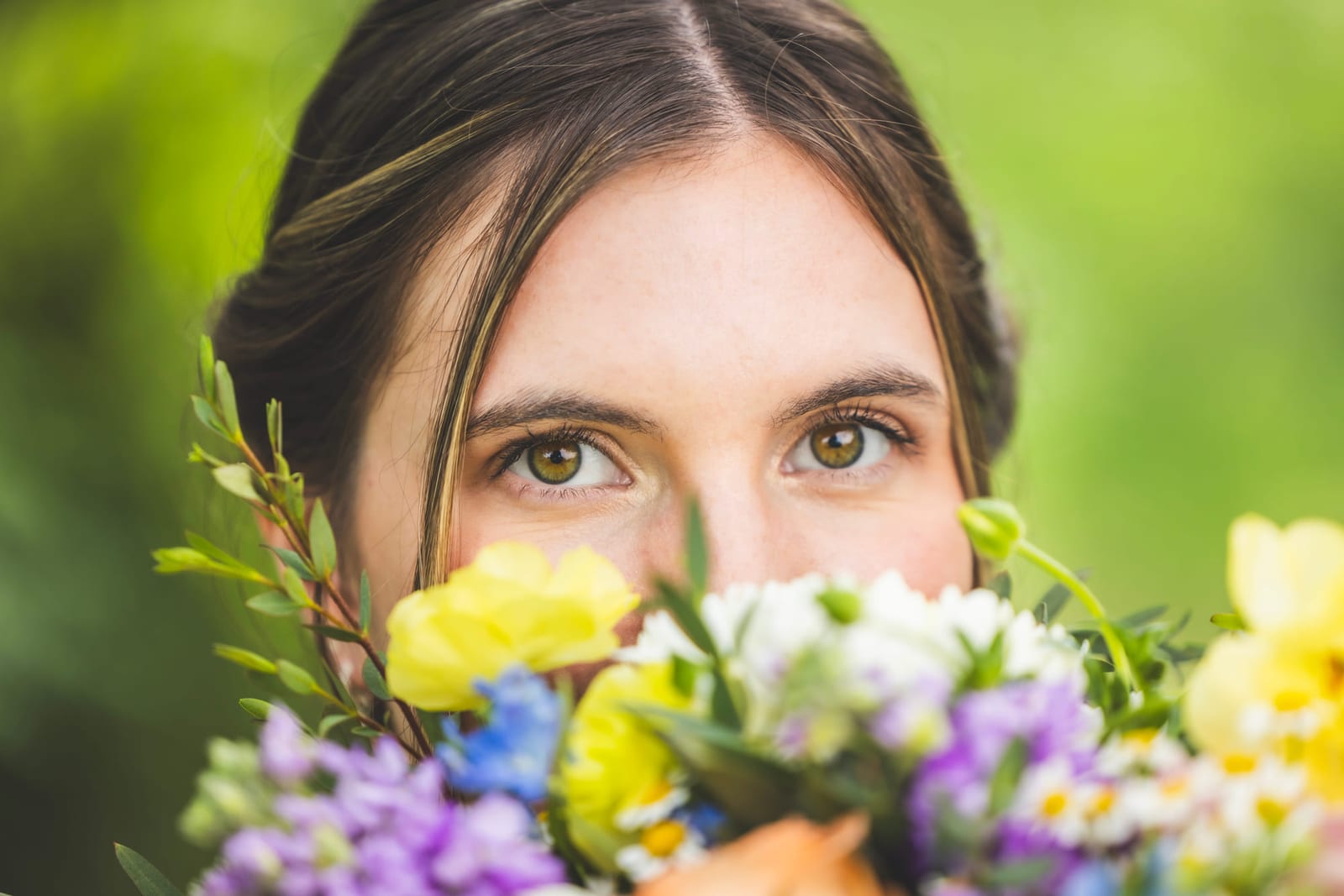 A close frame of a bride’s eyes above a bouquet of yellow and violet flowers.