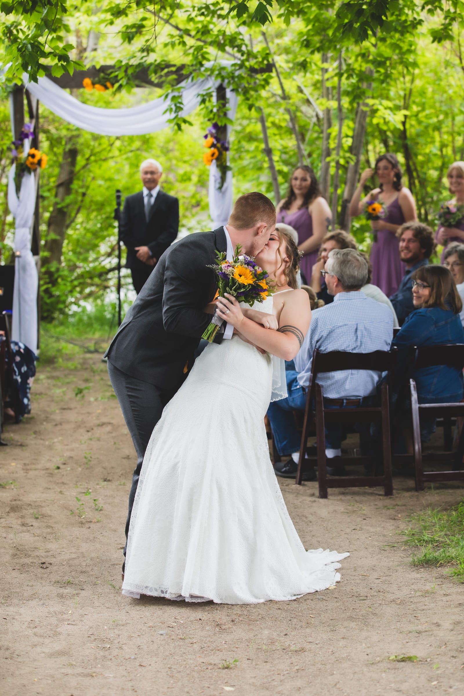 A groom dipping his bride at the end of the ceremony, seated guests and the officiant behind them.