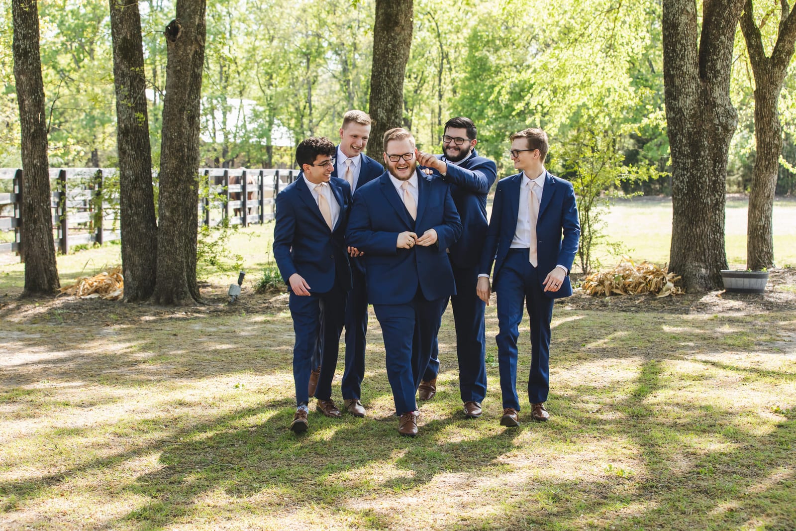 Groomsmen in navy walking together through a stand of trees.