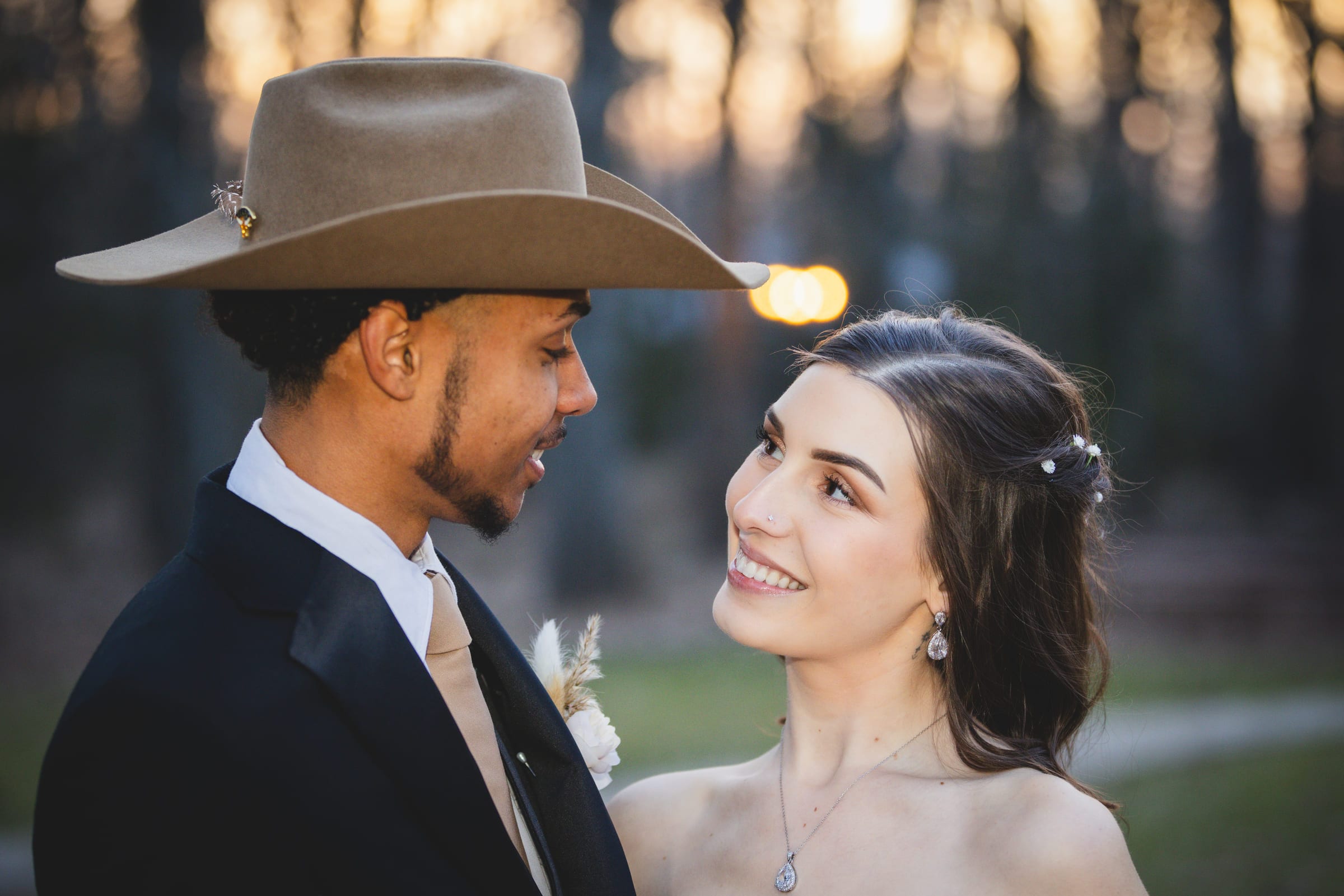 A groom in a wide-brimmed hat turned to face his bride, the two of them almost nose to nose in golden light.