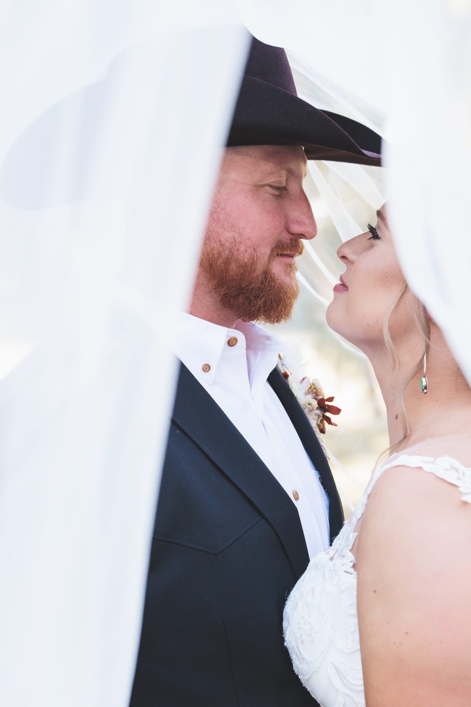 A couple looking at each other beneath the bride’s veil, drawn over them both like a tent.